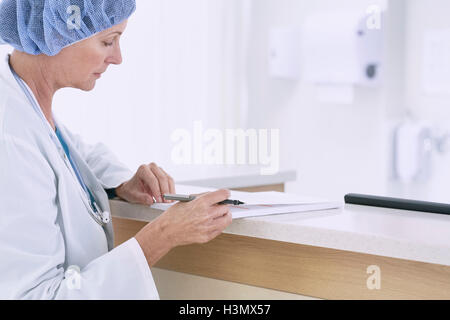 Medico donna la scrittura di note mediche a stazione di infermieri in ospedale Foto Stock