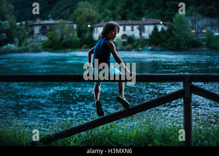 Ragazzo seduto sulla riga da fiume guardando sopra la spalla in telecamera Foto Stock