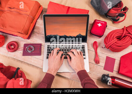 Vista aerea dell'uomo con le mani in mano la digitazione sul portatile mentre la preparazione di arrampicata attrezzature per il viaggio Foto Stock