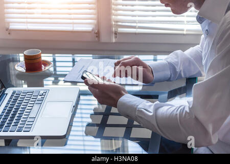 Imprenditore in ufficio lavoro interiore con il cellulare e il computer portatile con una tazza di caffè Foto Stock