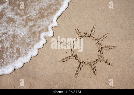 Sun disegnato sulla sabbia su una spiaggia con un'onda Foto Stock