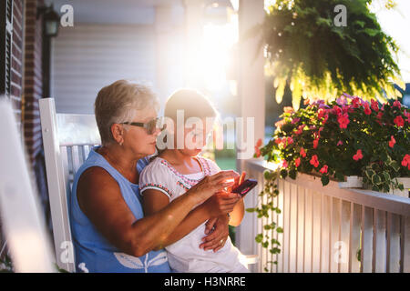 La ragazza e la nonna a giocare il gioco dello smartphone sulla veranda al tramonto Foto Stock