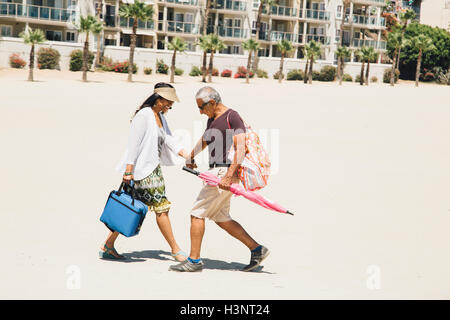 Coppia senior camminando sulla spiaggia, borse e zaini per picnic, Long Beach, California, Stati Uniti d'America Foto Stock