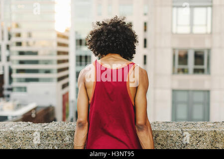 Vista posteriore del giovane uomo guardando giù dal tetto dei grattacieli Foto Stock