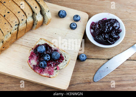 Vegetariano sesamo nero pane topping mirtillo marmellata di ribes e mirtilli freschi sulla tavola di legno Foto Stock