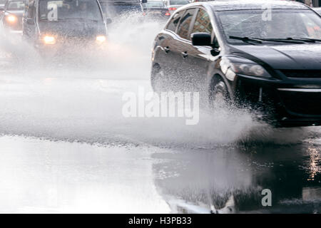 Sfocata flusso di auto durante la giornata piovosa. pioggia di spruzzi di acqua dalle ruote auto sulla strada allagata. Foto Stock