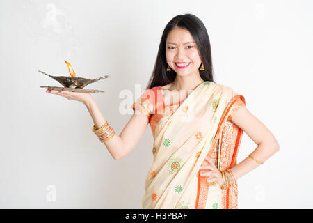 Ritratto di giovane razza mista cinese indiano femmina nel tradizionale sari abito, tenendo diya olio lampada luce, su sfondo semplice. Foto Stock
