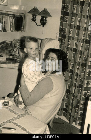Germania - circa sessanta: una donna con un bambino nelle braccia seduti vicino al tavolo da pranzo Foto Stock