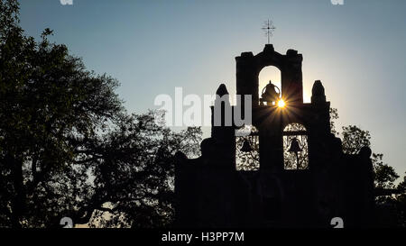 La missione spagnola Espada campane in silhouette come il sole tramonta dietro la missione di San Antonio, Texas Foto Stock