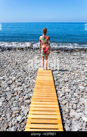 Donna in piedi sul percorso di legno a stony spiaggia e mare Foto Stock