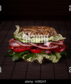Deliziosa e succosa burger con prosciutto, verdi, pomodori, pane con grani sullo sfondo di legno Foto Stock