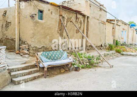 Il banco in casa sorge nella parte anteriore della casa con le travi a vista in legno proping fino la sua parete traballanti, Bukhara, Uzbekistan. Foto Stock