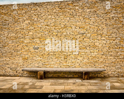 Un muro di pietra con panca in legno sede Foto Stock