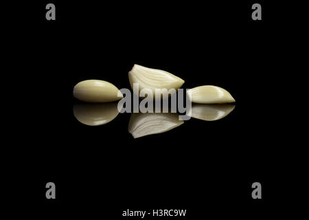 Tre aglio sbucciato isolato nero su sfondo riflettente Foto Stock