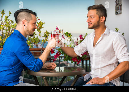 Vista laterale di due eleganti uomini belli seduti a tavola con bicchieri di vino mentre guardando faccia a faccia Foto Stock