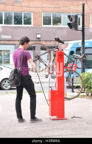 Giovane uomo pompare fino la sua moto pneumatici pneumatici a un pubblico bike stazione di riparazione stand al posto Emilie-Gamelin, Montreal city centre, Foto Stock