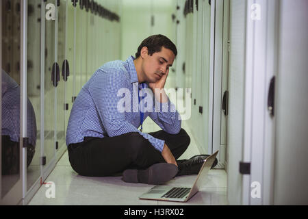 Ha sottolineato il tecnico seduto sul pavimento e guardando il computer portatile Foto Stock