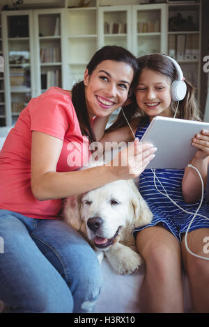 Felice madre e figlia seduti con il cane e ascolto di musica sulle cuffie Foto Stock