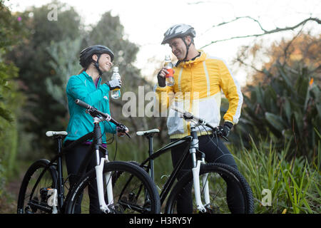Biker giovane in piedi con la bicicletta di acqua potabile nella foresta Foto Stock
