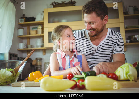 Padre e figlia sorridente ad ogni altro durante la preparazione di insalata Foto Stock