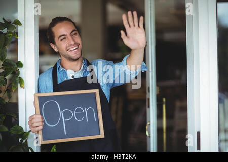 Cameriere in piedi presso il cafe porta azienda lavagna con segno aperto Foto Stock