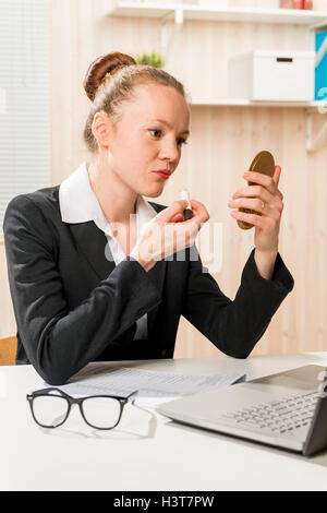 Business donna dipinge le labbra con il rossetto in office Foto Stock