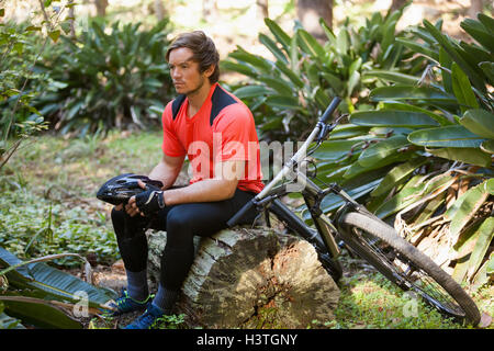 Esaurito maschio mountain biker rilassante su un tronco di albero nella foresta Foto Stock