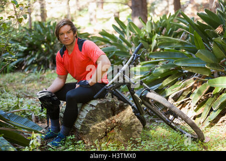 Ritratto di esaurito maschio mountain biker rilassante su un tronco di albero nella foresta Foto Stock