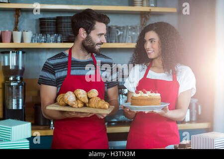 Cameriere e cameriera tenendo un vassoio di croissant e torte Foto Stock