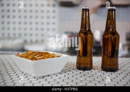 Bottiglie di birra e una ciotola di spuntini sul bancone bar Foto Stock