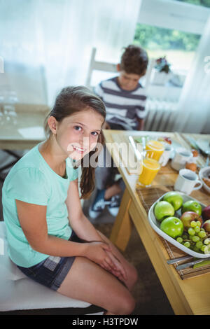 Ritratto di ragazza seduta sul tavolo da pranzo mentre il ragazzo in background Foto Stock