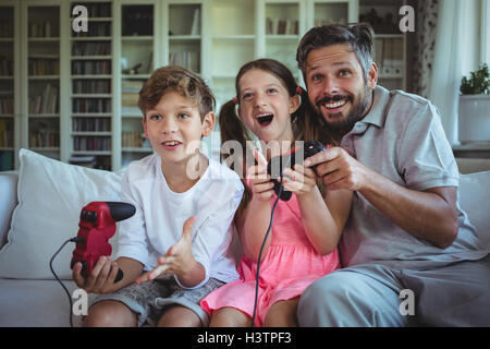 Padre seduto sul divano con i suoi figli e la riproduzione di video giochi Foto Stock
