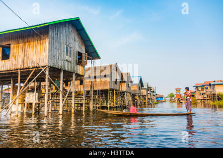 La barca di legno con la gente del posto nella parte anteriore della tradizionale palafitte sul Lago Inle, Nampan, Stato Shan, Myanmar Foto Stock