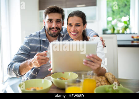 Giovane con tavoletta digitale mentre si consuma la colazione a casa Foto Stock