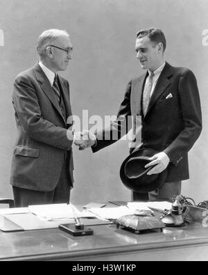 Negli anni Trenta due uomini in piedi alla scrivania in ufficio stringono le mani Foto Stock