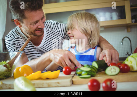 Padre e figlia sorridente ad ogni altro durante la preparazione di insalata Foto Stock