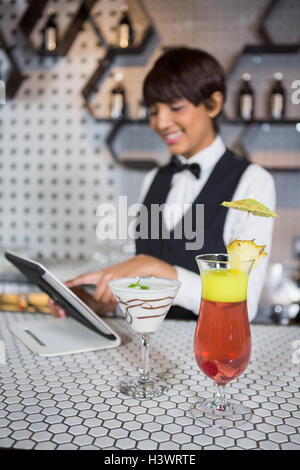 Cameriera utilizzando digitale compressa con un bicchiere di cocktail nel bar counter Foto Stock