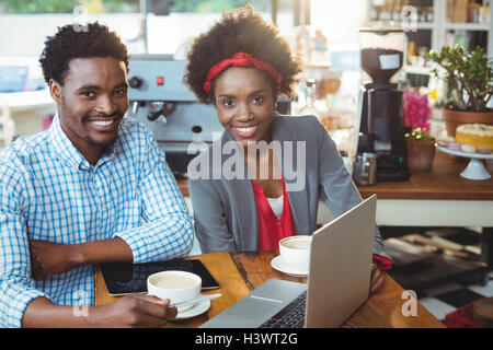 Uomo e donna che utilizza un computer portatile mentre avente tazza di caffè Foto Stock