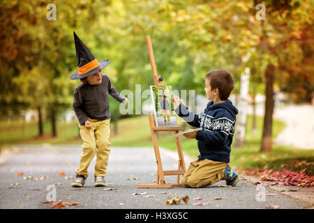 Due dolci bambini, ragazzo fratelli, avendo divertimento pittura in autunno park insieme. Un bambino di dipingere il altro capretto, collata per santificare Foto Stock