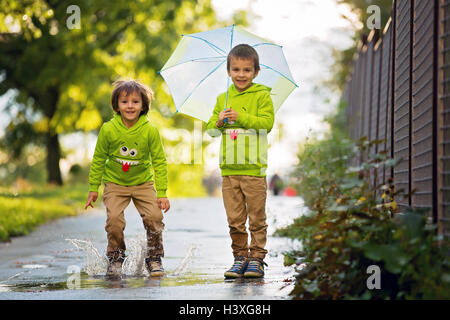 Due adorabili poco ragazzi con ombrello in un parco in un giorno di pioggia, giocando e saltando, sorridente, parlare insieme, autumntime Foto Stock