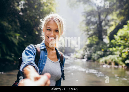 Sorridente giovane donna azienda mano d'uomo e conduce a lui nella foresta escursione. Punto di vista colpo di coppia da parte del creek. Foto Stock