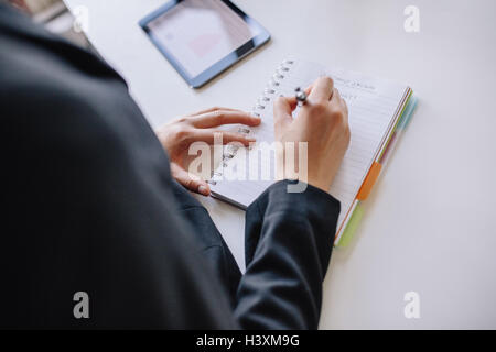 Immagine ravvicinata di giovane imprenditrice mani la scrittura su notepad presso l'ufficio. Femmina di prendere appunti in un libro. Foto Stock