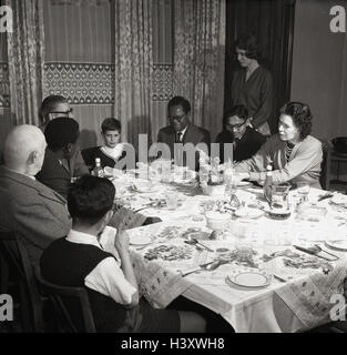 Degli anni Cinquanta, storico gruppo di persone di diverse generazioni e nationalties sedersi a un tavolo insieme avente un pasto. Foto Stock