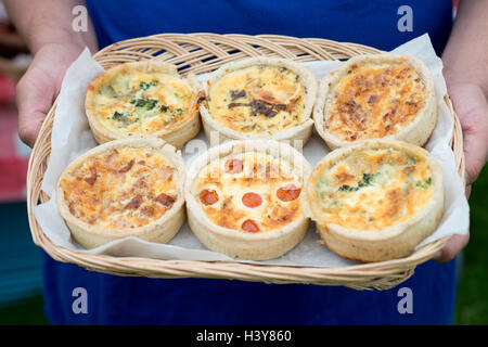 Close up orizzontale colpo di piccolo cesto detenute da Le Mans mani contenente sei gustosa quiche con vari ripieni Foto Stock