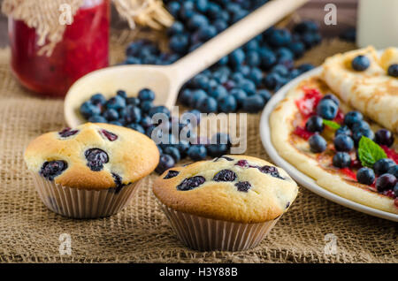 Muffin ai mirtilli latte e inceppamento in background e cesto pieno di mirtilli Foto Stock