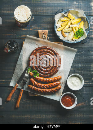 Salsicce alla griglia, patate arrosto e birra scura su sfondo di legno Foto Stock