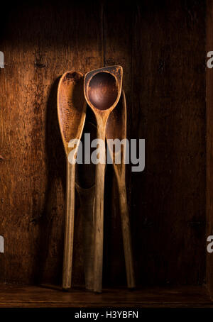 Cucchiaio di legno insieme con legno scuro dello sfondo. Retrò utensili da cucina rustica con texture usurati. Foto Stock