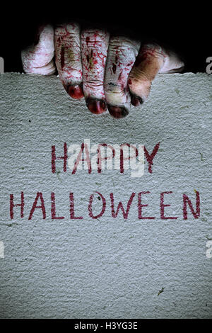 Primo piano di Halloween e la mano di un uomo non morti tenendo un cartello con scritto il testo happy Halloween scritto in esso Foto Stock