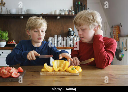 Ragazzo che assiste il fratello per tritare il peperone a tavola in cucina Foto Stock