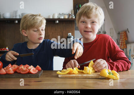 Ritratto di disabilitato ragazzo seduto con il fratello a tavola con verdure in cucina Foto Stock